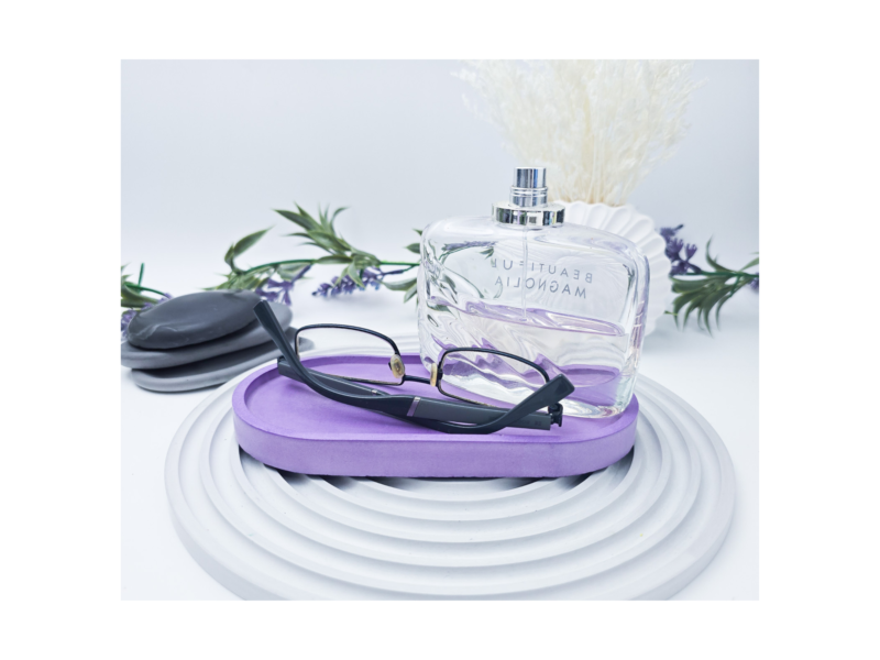 Perfume bottle resting on a purple flip-flop, with glasses laid over the sandal and botanical décor in the background.