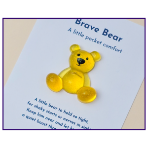 Yellow teddy bear on a page that reads 'Brave Bear: A little pocket comfort' with purple border framing the image.