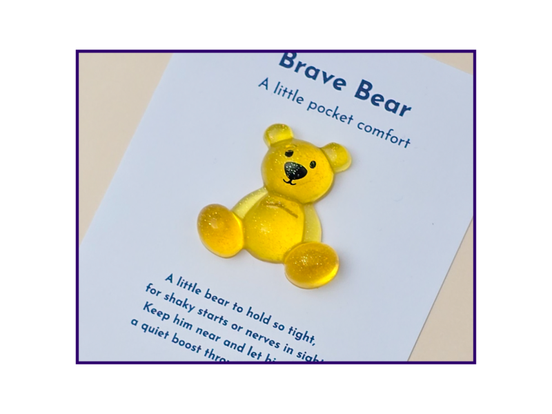 Yellow teddy bear on a page that reads 'Brave Bear: A little pocket comfort' with purple border framing the image.