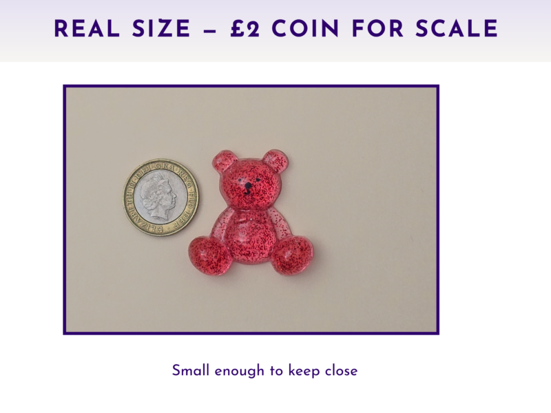 Small pink glitter bear figurine beside a £2 coin on a light surface to show scale.