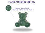 Green teddy bear sculpture with a smooth, glossy, mottled finish; a circular zoom inset in the upper left shows the texture, connected by a purple line, with text that reads 'Hand-finished detail' at the top of the image.