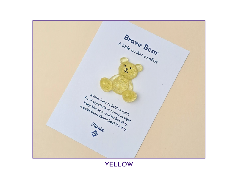 Glittery yellow teddy bear attached to a white card with Brave Bear branding and the slogan 'A little pocket comfort'.