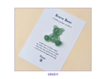 White product card titled 'Brave Bear' with a green glitter bear attached, on a pale background; reads 'A little pocket comfort' and includes a short poem.
