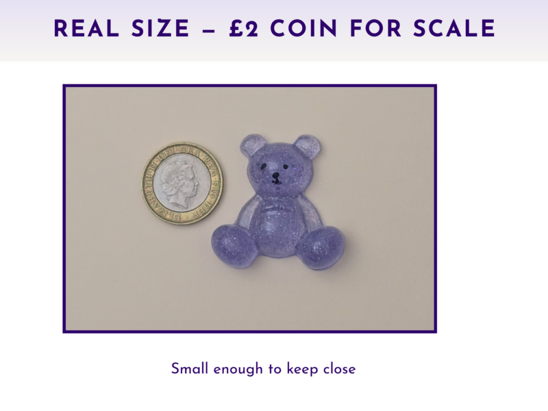 Purple glitter teddy bear figure beside a UK two-pence coin on a light surface, showing scale for size comparison.