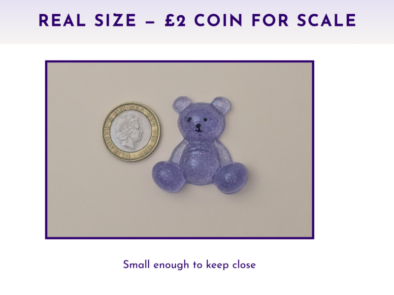 Purple glitter teddy bear figure beside a UK two-pence coin on a light surface, showing scale for size comparison.