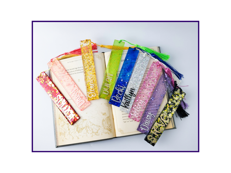 KXK-RBMK-01 Colorful glittery bookmarks with tassels laid across an open book.
