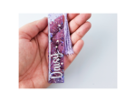 KXK-RBMK-03 Close-up of a hand holding a purple glittery tassel bookmark against a light background, showing sparkles on the bookmark surface.