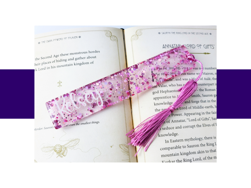 Open book with ornate page margins and a pink glitter bookmark laid across the pages.