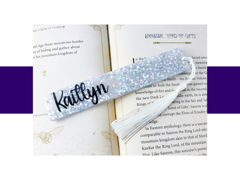 Open fantasy book with a glittery silver star-pattern bookmark and white tassel laid across the pages.