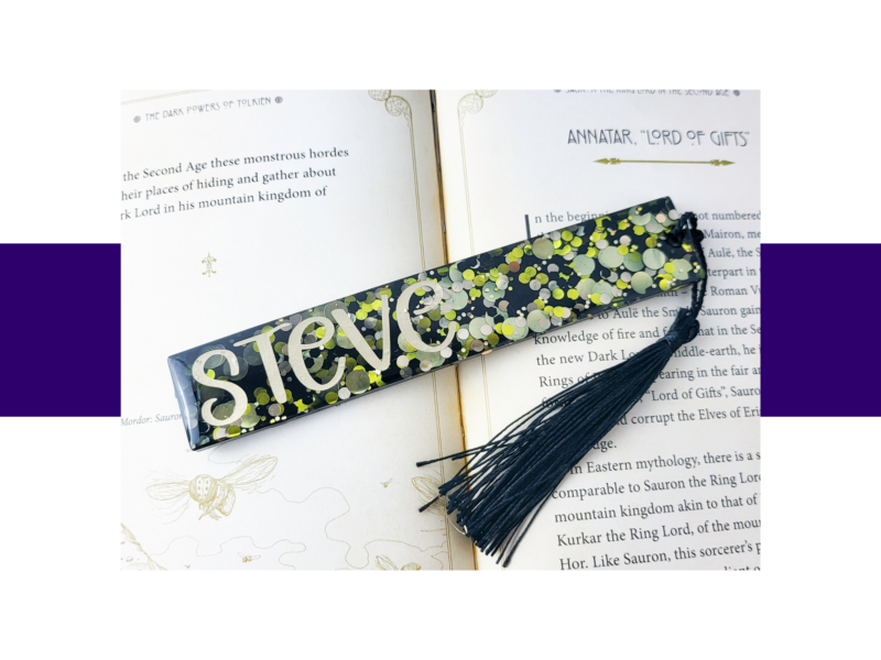 Open book pages with a colorful glittery bookmark lying across the spread, tassels visible at the edge.