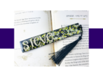 Open book pages with a colorful glittery bookmark lying across the spread, tassels visible at the edge.
