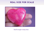 Close-up of a glittery pink heart being held between two fingers against a purple background, showing its size for scale.