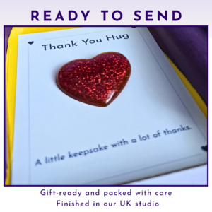 Close-up of a card showing a glittery red heart and the words 'Thank You Hug' on a page inside a gift package, suggesting a thoughtful keepsake gift