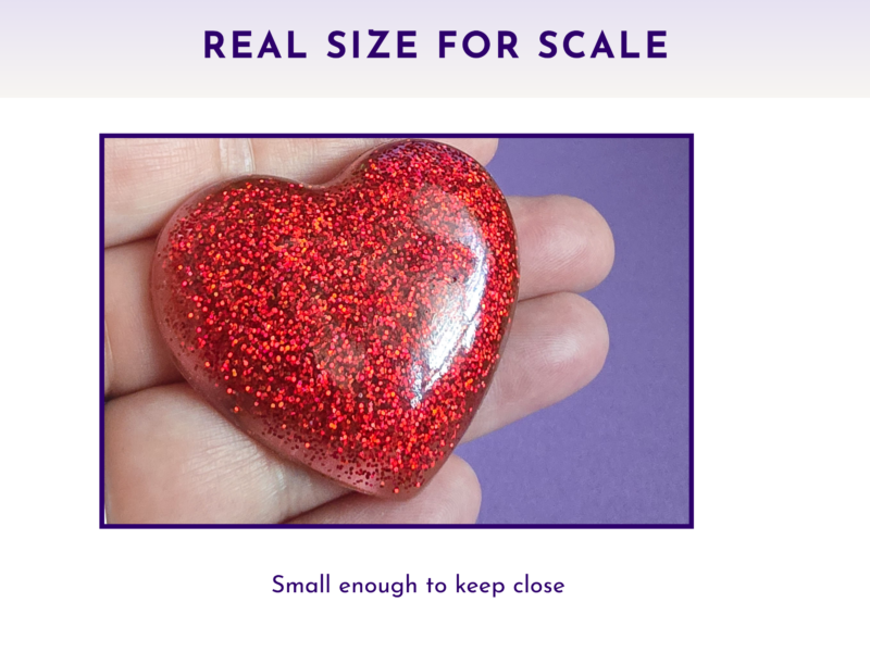 Shiny red glitter heart held between fingers against a purple background