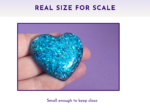Blue glitter heart held between fingers against a purple background, suggesting a small keepsake.