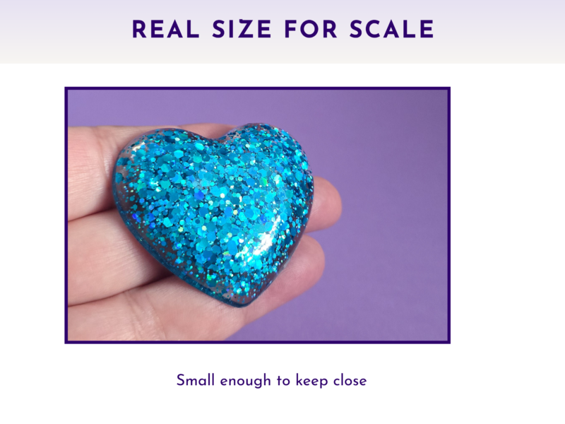 Blue glitter heart held between fingers against a purple background, suggesting a small keepsake.