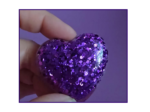 Close-up of a finger pinching a purple glittery ball against a purple background and lighting that highlights the sparkles.