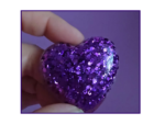 Close-up of a finger pinching a purple glittery ball against a purple background and lighting that highlights the sparkles.