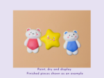 KNP-PYO-BEARS-mini_033. Painted result Three smiling clay figures—a pink-dressed bear, a yellow star, and a blue-dressed bear—on a peach background.