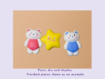 Three smiling clay figures—a pink-dressed bear, a yellow star, and a blue-dressed bear—on a peach background.