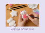 KNP-PYO-BEARS-mini_066. Main benefit Hands paint a white bear figurine with pink apron on a wooden table, surrounded by brushes and craft supplies.