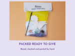 Ready-to-give craft kit with paints, brush, white dinosaur cutout, yellow package, and purple shredded paper inside a clear bag on an orange background.