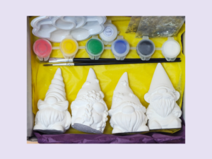 White ceramic figurines arranged with a paint set (red, yellow, green, blue, gray, white), glue, and brushes on a yellow craft tray