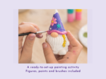 Hands painting a small ceramic gnome with a purple hat and pink flower accents.