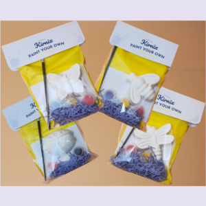 DIY paint kits with yellow packaging and white butterfly shapes, scattered paint pots and brushes on a purple backdrop
