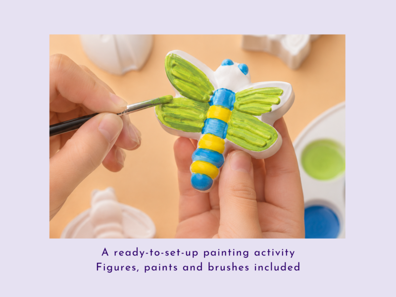 Close-up of hands painting a white ceramic butterfly with bright green wings using a small brush.