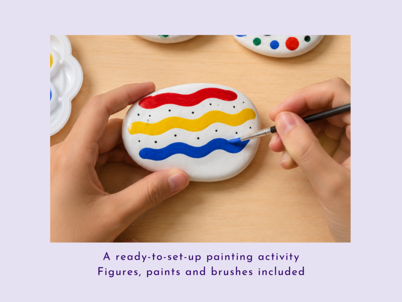 Hands painting a white egg with red, yellow, and blue wavy stripes on a wooden table.