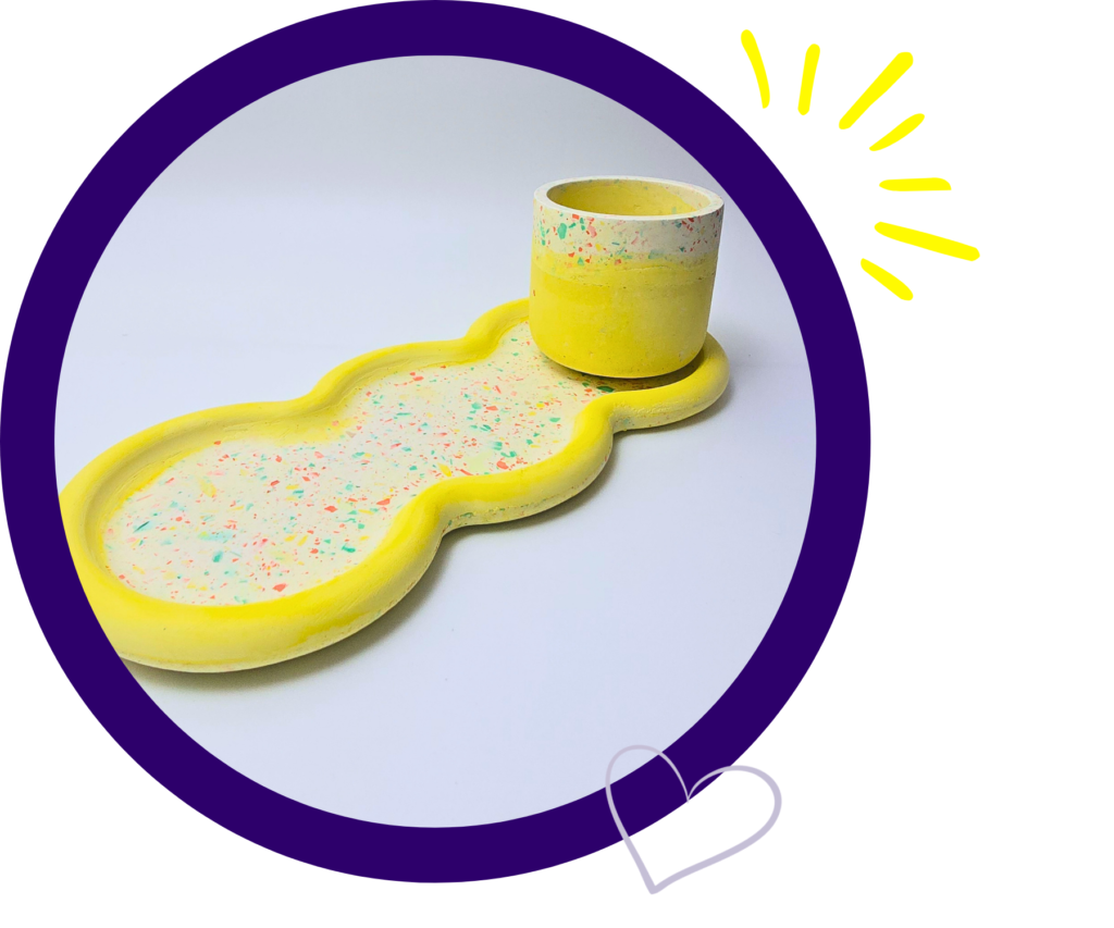 Yellow speckled cake-sculpture shaped like a pipe inside a thick purple circular frame with a yellow sunburst on white background (decorative image)