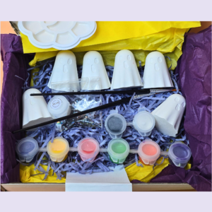 Six unpainted white eco resin ghost figures in an orange gift box with blue shredded tissue and a Kirnix paint your own label, photographed on an orange background
