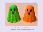Two bright ghost-shaped gourds, one green and one orange, stand side by side on a pale surface as a craft display.