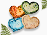 Decorative image of overlapping, colorful heart-shaped rocks in orange, green, blue, and beige, with fern fronds around them on a white background.