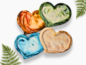 Decorative image of overlapping, colorful heart-shaped rocks in orange, green, blue, and beige, with fern fronds around them on a white background.