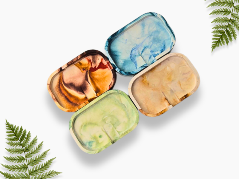 Watercolor paint palettes in pastel colors arranged diagonally with fern fronds in the corners.