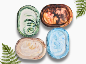 Set of marbled soaps in green, brown, peach, and blue with fern sprigs on a white background (top-down view).