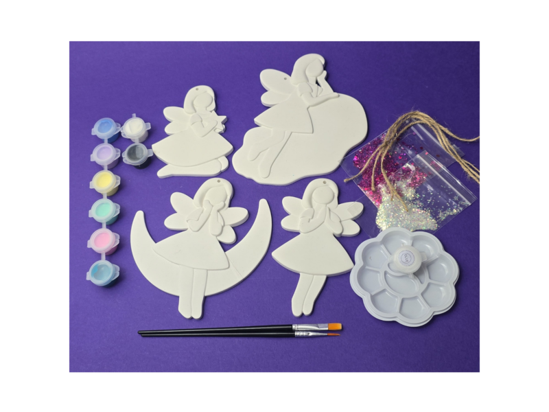White angel-shaped craft cutouts with glitter, paints, and brushes on a purple background (craft supplies).
