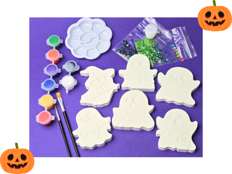 Assorted Halloween craft supplies on a purple background: ghost shapes, glitter, and small paint pots with brushes, framed by pumpkin corners.
