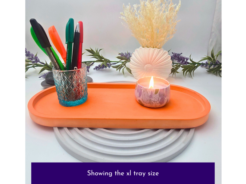 Orange tray with a glass pen holder full of colorful pens, a lit patterned candle cup, and dried flowers with lavender garlands in the background.