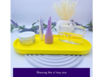 Assorted skincare and fragrance items arranged on a bright yellow tray with lavender sprigs and a clear perfume bottle against a plain background.