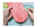 Two hands hold a pink rubber sandal over a blue textured surface, likely for cleaning or inspection.